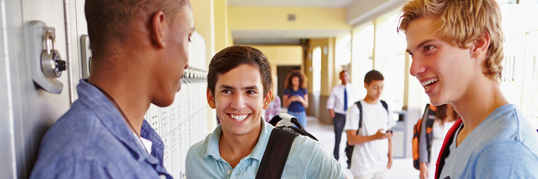 High school students talk near some lockers in a school hallway.